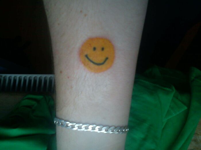 Colorful smiley face tattoo on a hand, showcasing funny tattoo art.