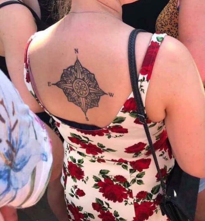 Compass tattoo on woman's back in floral dress, showcasing funny tattoo design.