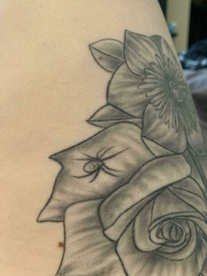 Funny tattoo of a realistic spider on a petal amidst floral design.