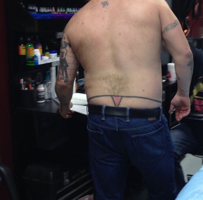 Man with funny tattoo of underwear waistband on lower back standing in a tattoo studio.