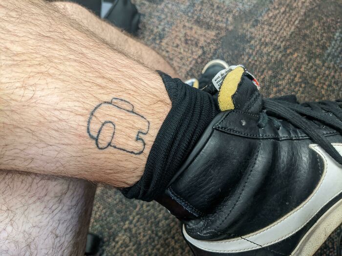Funny tattoo of an Among Us character peeking from behind a sock on a leg.