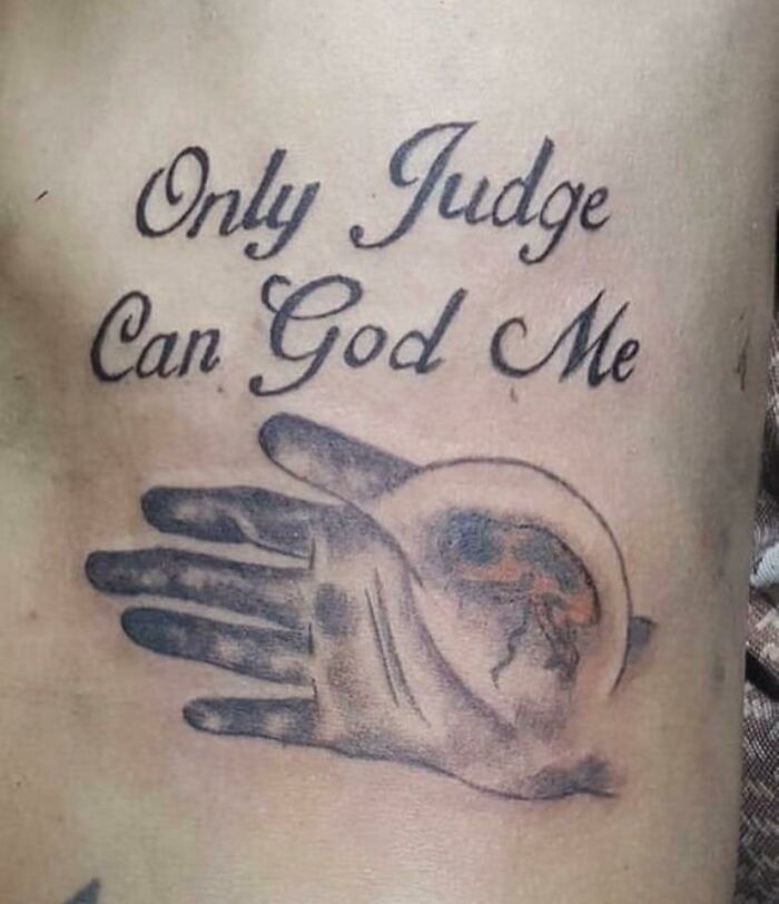 Funny tattoo with text "Only Judge Can God Me" and an image of a hand holding a brain, intended to humorously confuse.