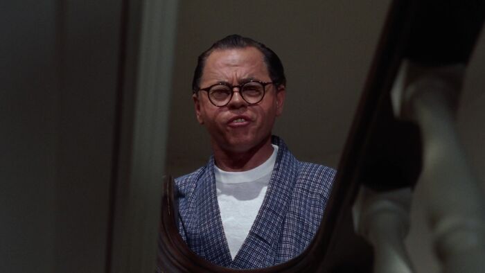 Mickey Rooney wearing a white t-shirt and checkered robe in Breakfast at Tiffany, one of the famous people married multiple times.