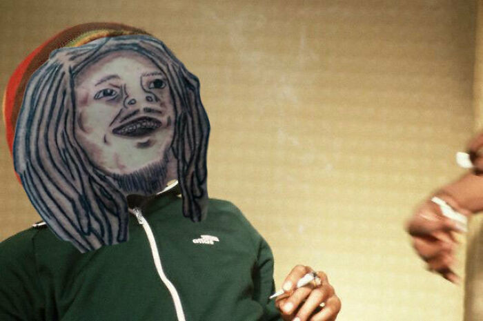 Terrible tattoo on someone's face, poorly executed compared to an original design, smoking in a dimly lit room.