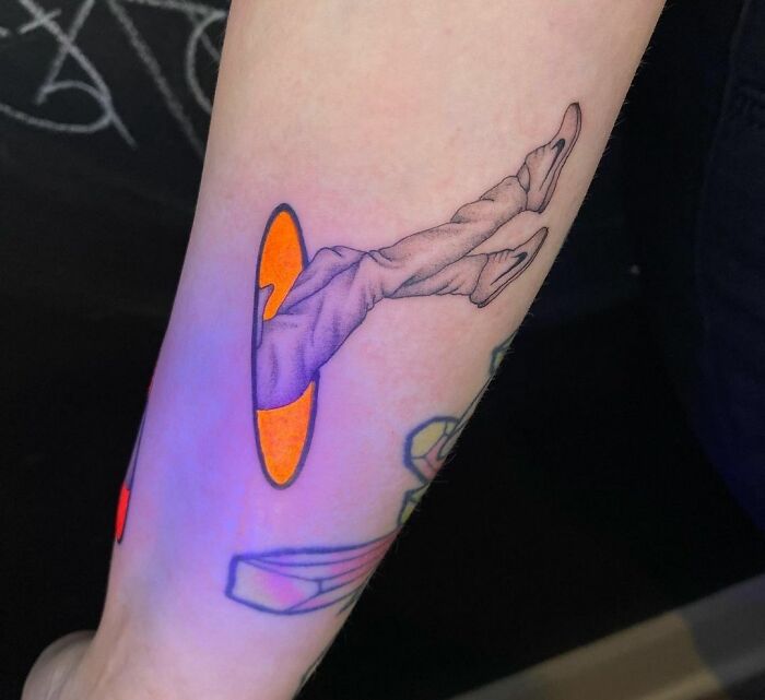 Trippy tattoo of legs emerging from a vortex, creating an optical illusion on an arm.