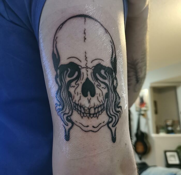 A trippy tattoo of a melting skull on an arm, with surreal and fluid design details.