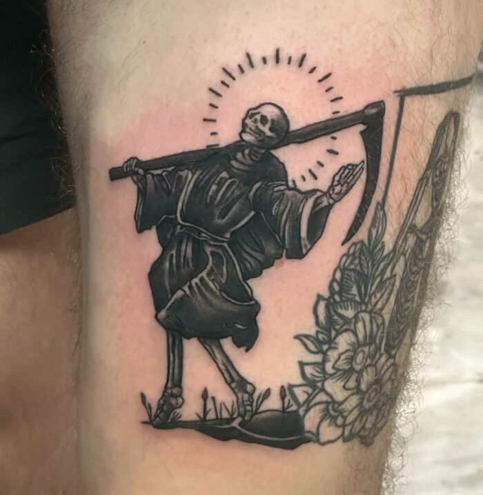 A trippy tattoo featuring a skeleton in a robe with a scythe, surrounded by a halo on a person's arm.