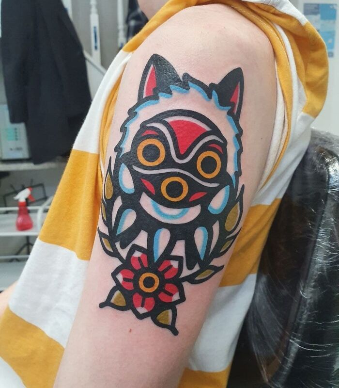 Colorful trippy tattoo of abstract animal design on a person's upper arm, with a striped yellow and white shirt.