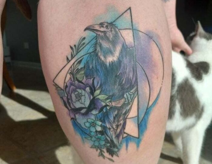 Trippy tattoo of a raven with geometric shapes and floral elements in vibrant colors on someone's leg.