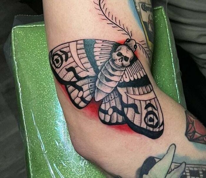 A trippy tattoo of a moth with a skull on its back, designed in a bold style on an arm.