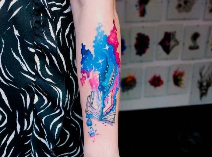 Colorful trippy tattoo on forearm with an open book and cosmic design.