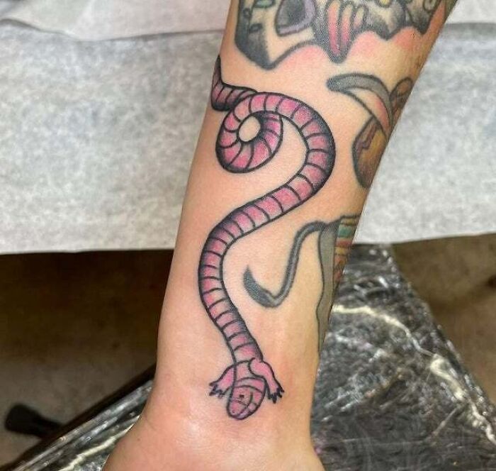 A trippy tattoo of a pink snake with a spiral pattern wraps around the forearm.