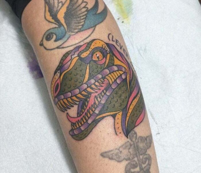 Trippy tattoo of a colorful dinosaur head with surreal patterns on an arm, featuring vibrant colors and intricate details.