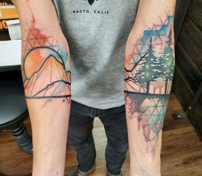 Colorful trippy tattoos featuring mountains and trees on forearms, blending geometric and watercolor styles.