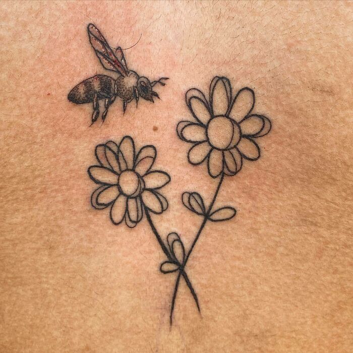 Bee hovering over daisy flowers tattoo, symbolizing mother-child bond.