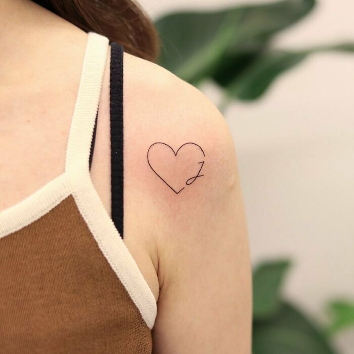Minimalist mom tattoo on shoulder, featuring a heart outline with a stylized initial, symbolizing the mother-child bond.
