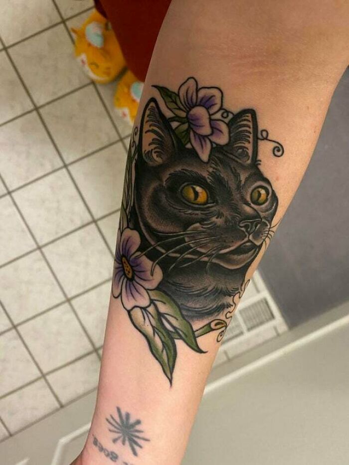Cat tattoo with flowers on a forearm, symbolizing mom and child bond.