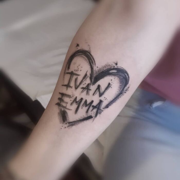Arm tattoo with a heart design featuring the names "Ivan" and "Emma," symbolizing the mother-child bond.