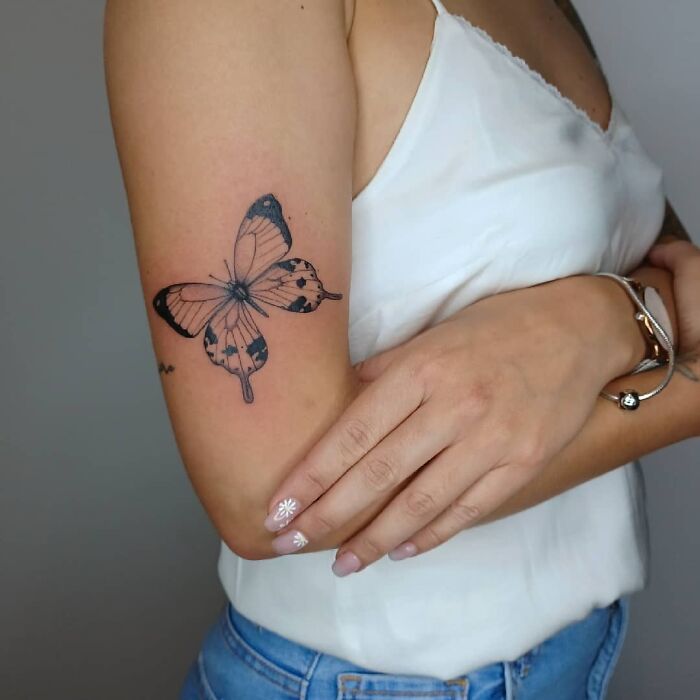 Butterfly mom tattoo on a woman's upper arm, symbolizing the mother-child bond in a simple, elegant design.