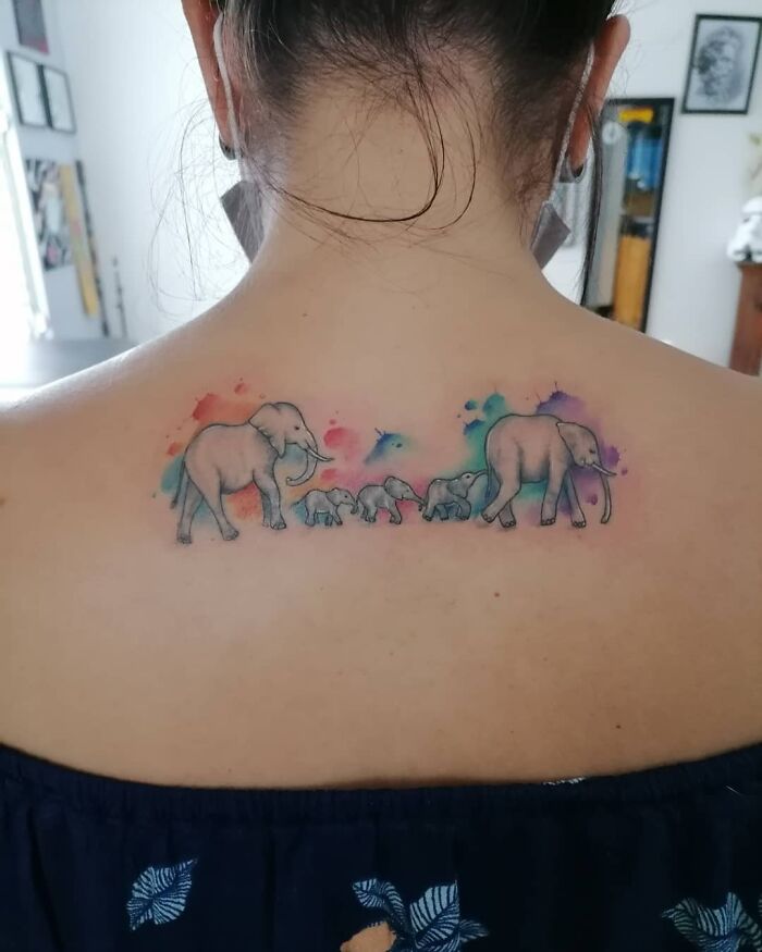 Elephant family tattoo on back symbolizes mother-child bond with colorful watercolor accents.