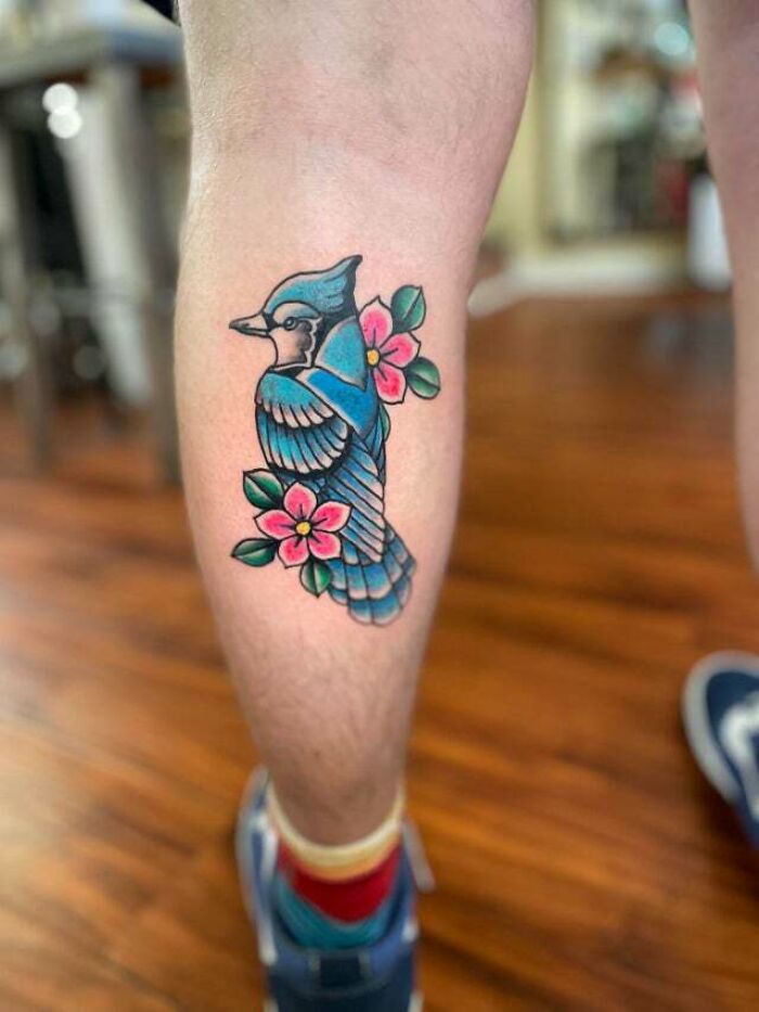 Bluebird tattoo with pink flowers on a leg, symbolizing beautiful mom tattoo ideas and the mother-child bond.