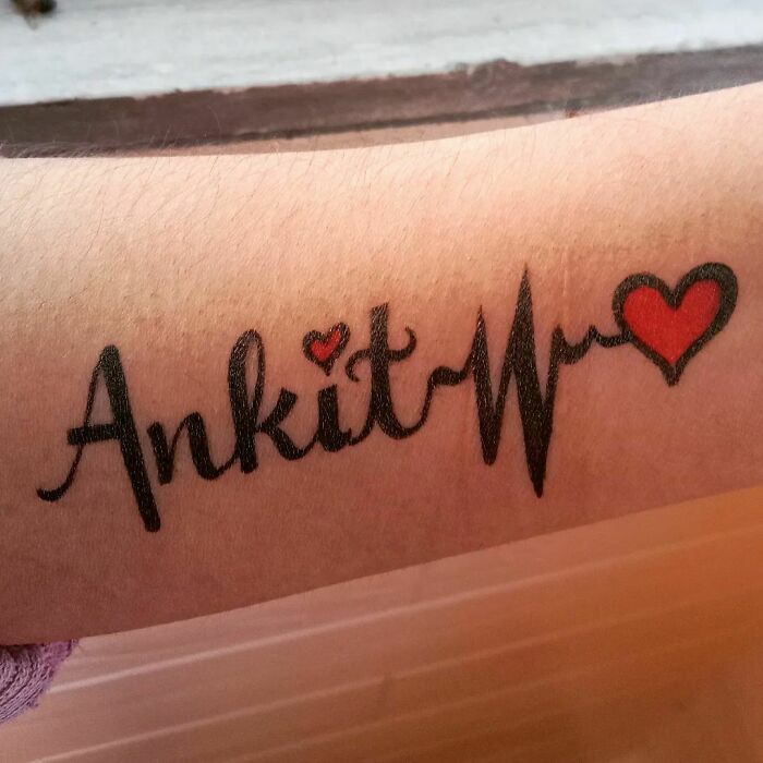 Arm tattoo featuring "Ankit" with a heartbeat line and heart, symbolizing the mother-child bond.