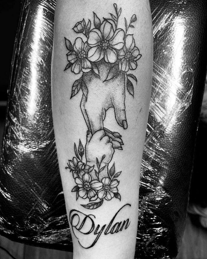 Mother-child bond tattoo featuring hands entwined with flowers and the name "Dylan" in elegant script.