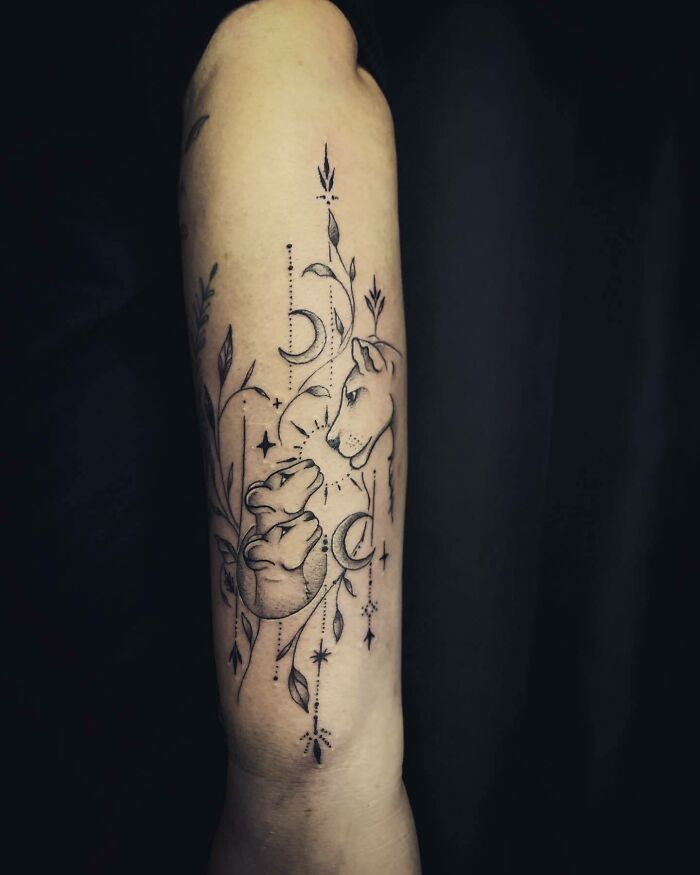 Lion and cub tattoo on arm, symbolizing the mother-child bond with celestial elements and floral designs.