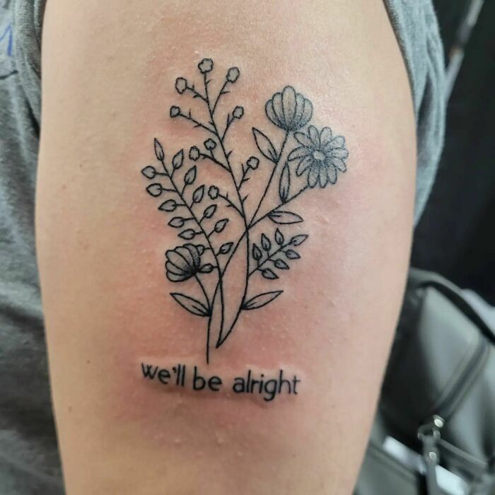 Floral tattoo on arm with "we'll be alright" text, symbolizing mom-child bond.