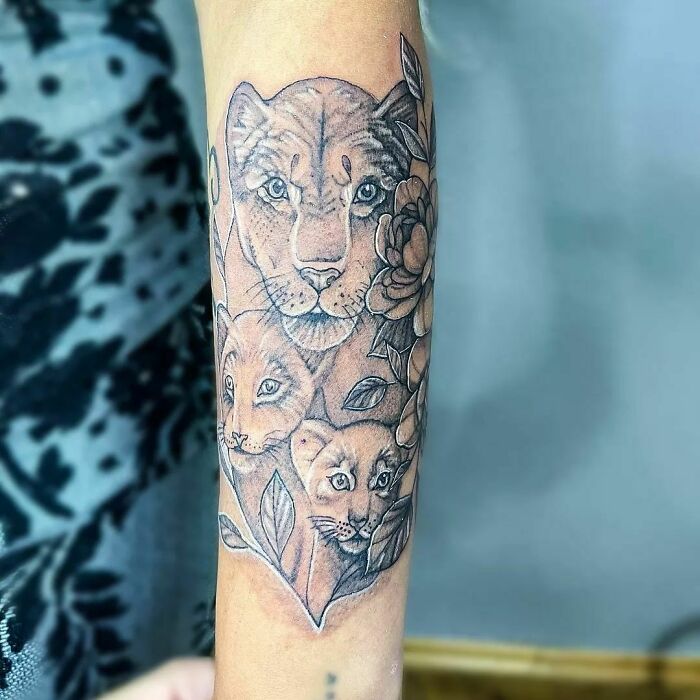 Lioness and cubs tattoo symbolizes mom-child bond with floral elements, beautifully detailed on forearm.