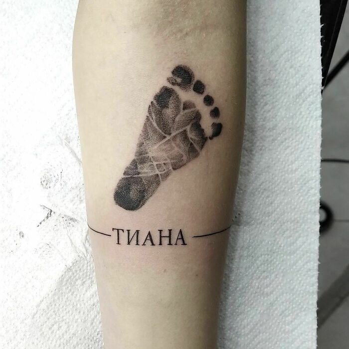 Tattoo of a baby's footprint on arm with name underneath, representing the mother-child bond.