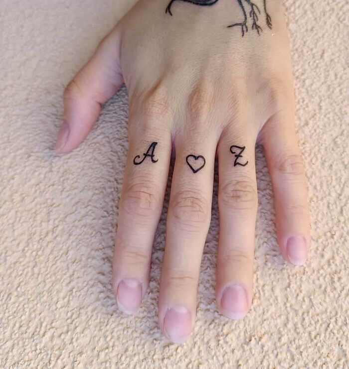 Hand with small finger tattoos of letters and heart symbol, showcasing a mom tattoo idea.