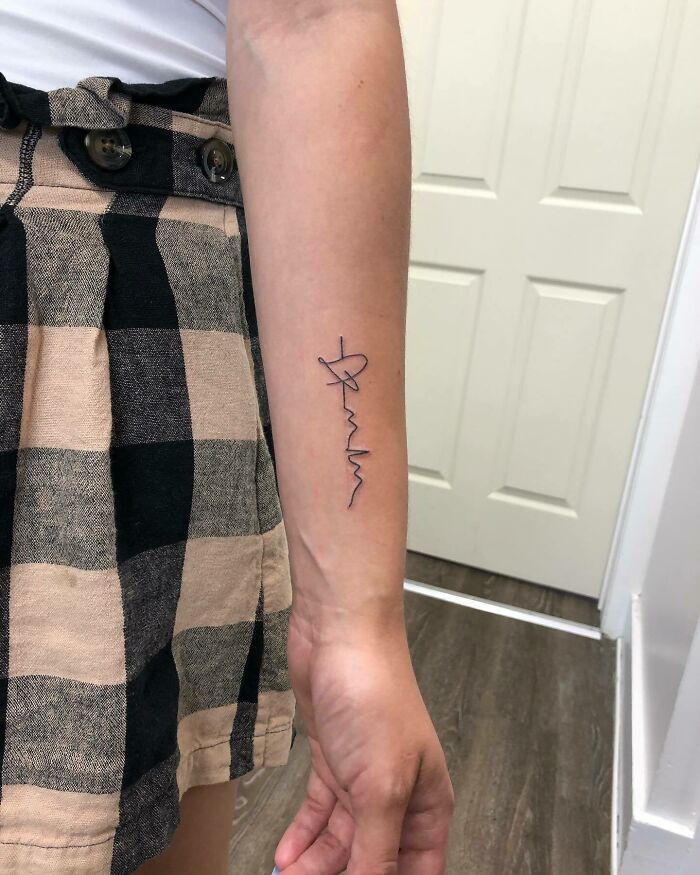 Minimalist mom tattoo in black ink on forearm, showcasing a mother-child bond.