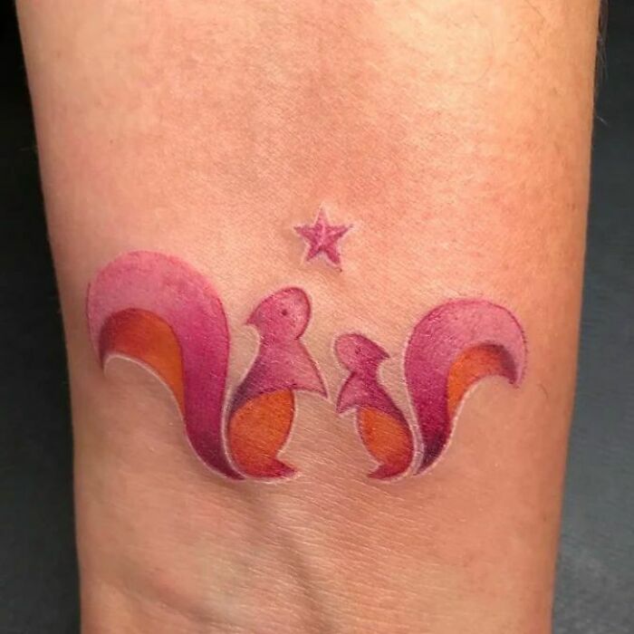 Mom tattoo featuring two stylized squirrels in pink and orange, symbolizing mother-child bond, with a small star above.