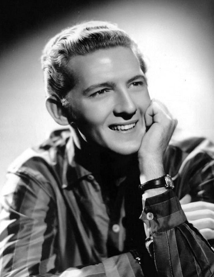 Jerry Lee Lewis smiling in a striped shirt, one of the famous people who got married multiple times, in a classic black and white photo.