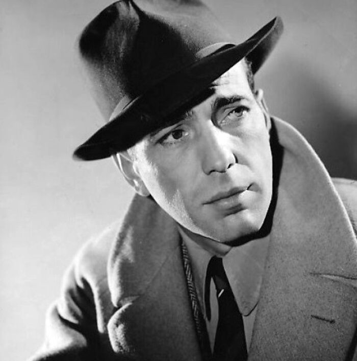 Humphrey Bogart wearing a black hat and coat, classic portrait of a famous person known for multiple marriages.