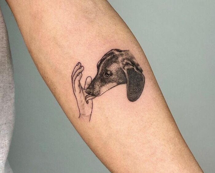 Pet tattoo of a dog's head with a hand on a person's forearm.