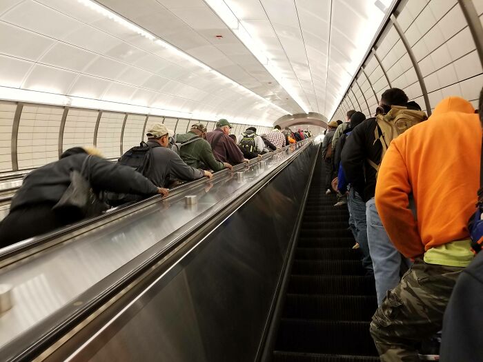 Crowded New York subway escalator with diverse commuters heading up in a busy urban transit scene.