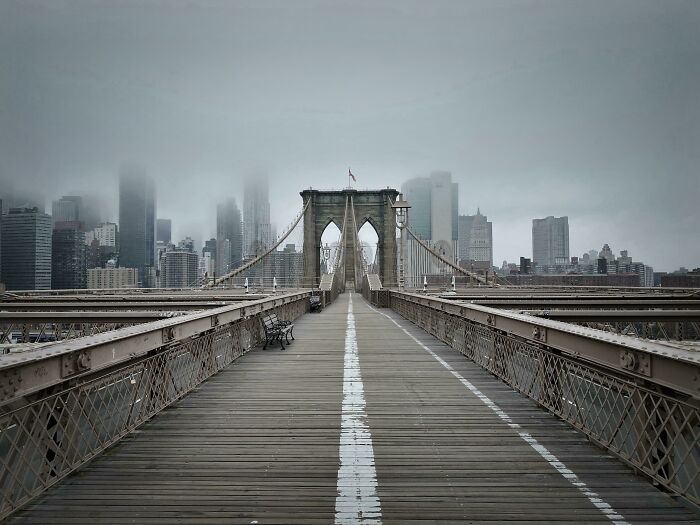 Brooklyn Bridge walkway in New York City with foggy skyline, illustrating unique and iconic New York cityscape views.