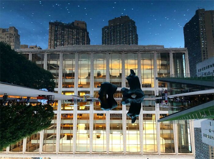 Night view of New York City with reflective modern building and unique sculptures, showcasing how New York is unlike any other city.