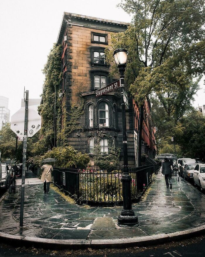 Rainy New York street corner with ivy-covered brownstone and pedestrians holding umbrellas on Stuyvesant Street.