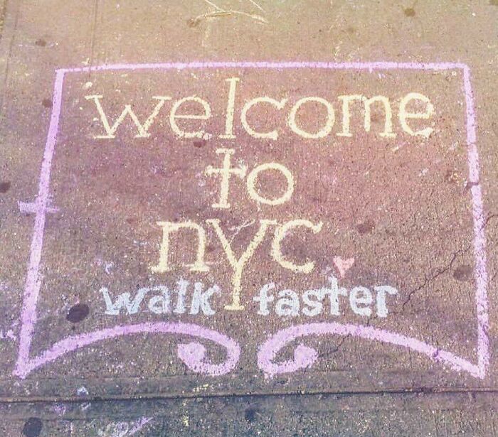 Chalk drawing on sidewalk in New York City reading welcome to nyc walk faster, showcasing NYC humor.