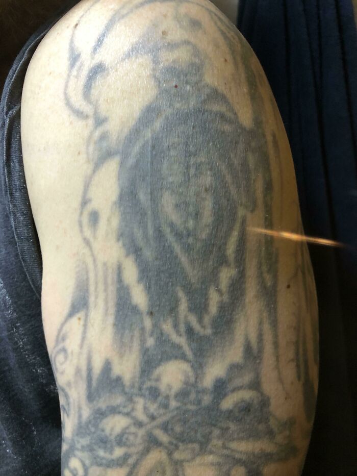 Aged tattoo on an upper arm showing faded ink and blurred outlines over the years.