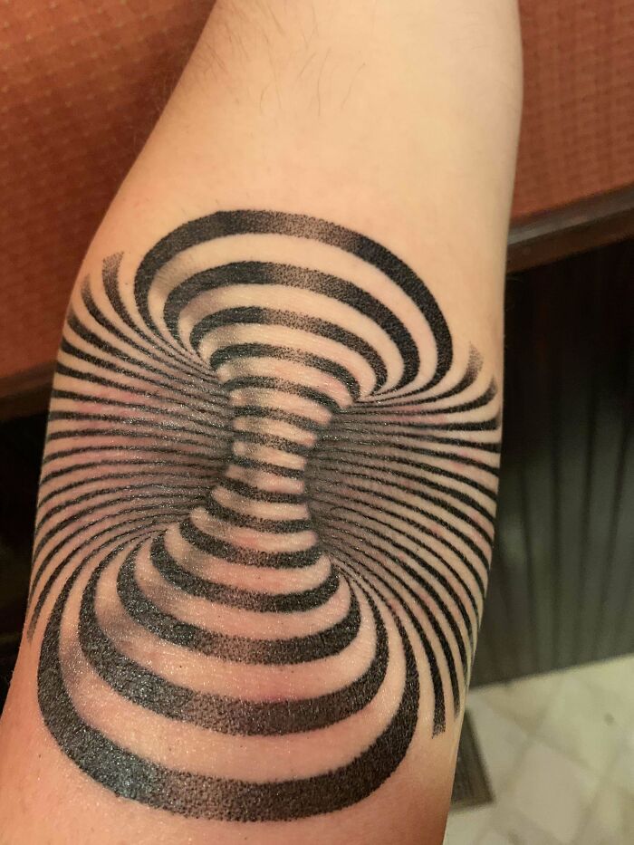 Optical illusion tattoo on an arm with curving black lines creating a mind-bending three-dimensional effect.