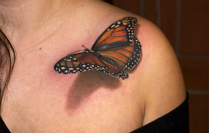 Optical illusion tattoo of a realistic butterfly on shoulder, creating a 3D effect.