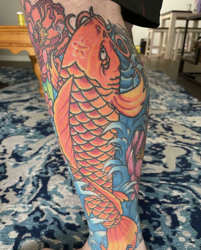 Colorful aged koi tattoo on leg, vibrant orange and blue, showcasing intricate detail and how tattoos change over time.