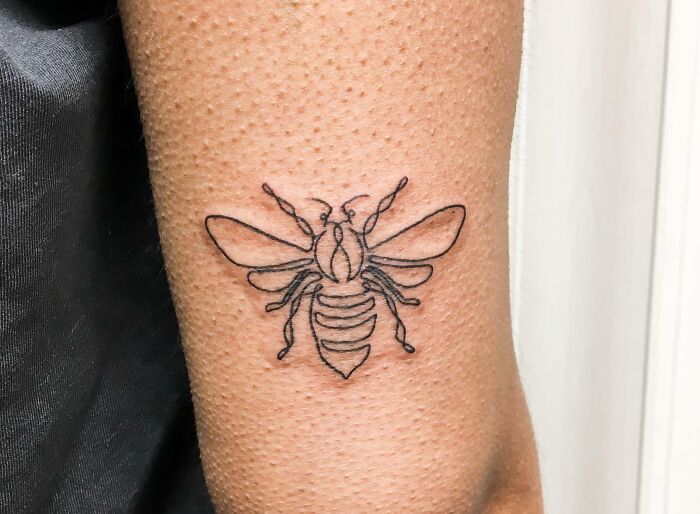 Minimalist line tattoo of a bee on an arm, showcasing unique ink art for minimalism enthusiasts.
