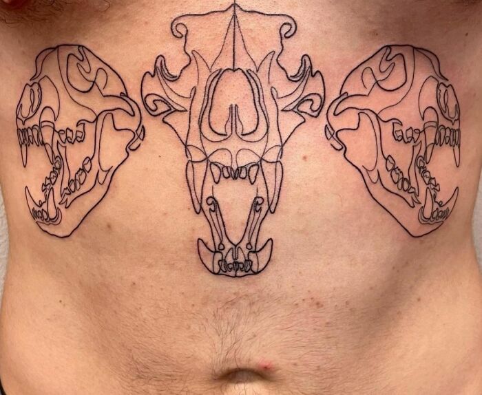 Minimalist line tattoo of three animal skulls on torso.