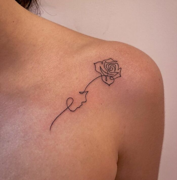 Minimalist line tattoo of a rose and face design on a person's shoulder, emphasizing simplicity and elegance.