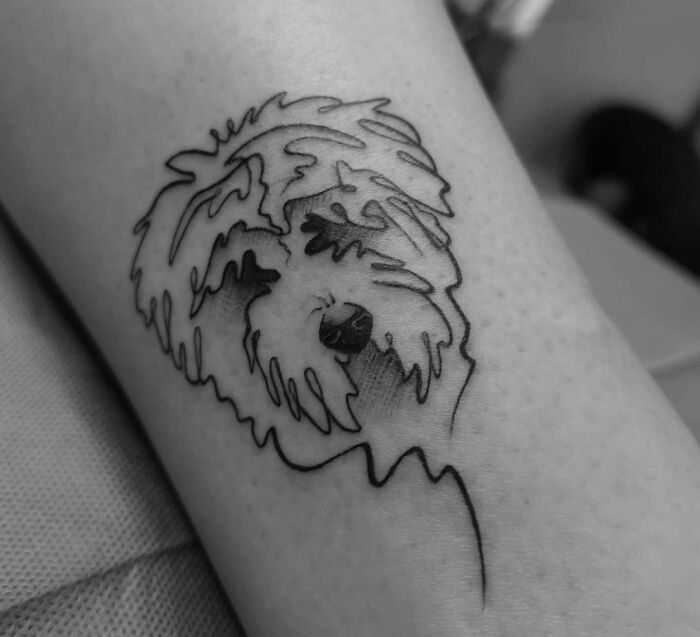 Minimalist line tattoo of a dog's face on an arm.